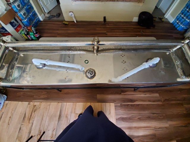 A person is standing next to a stainless steel sink on a wooden floor.