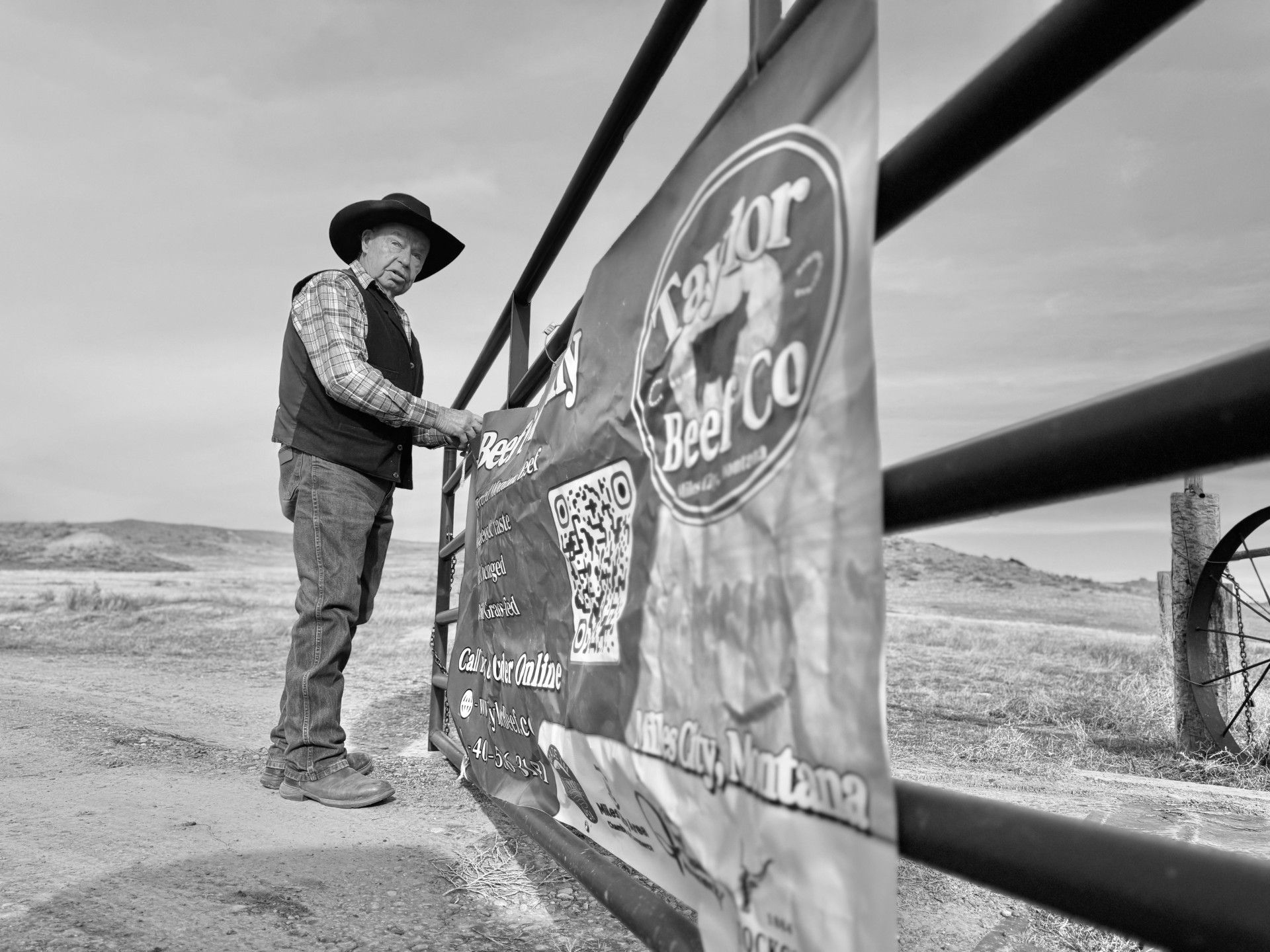 Man in cowboy hat attaching a banner to a fence in a rural field.