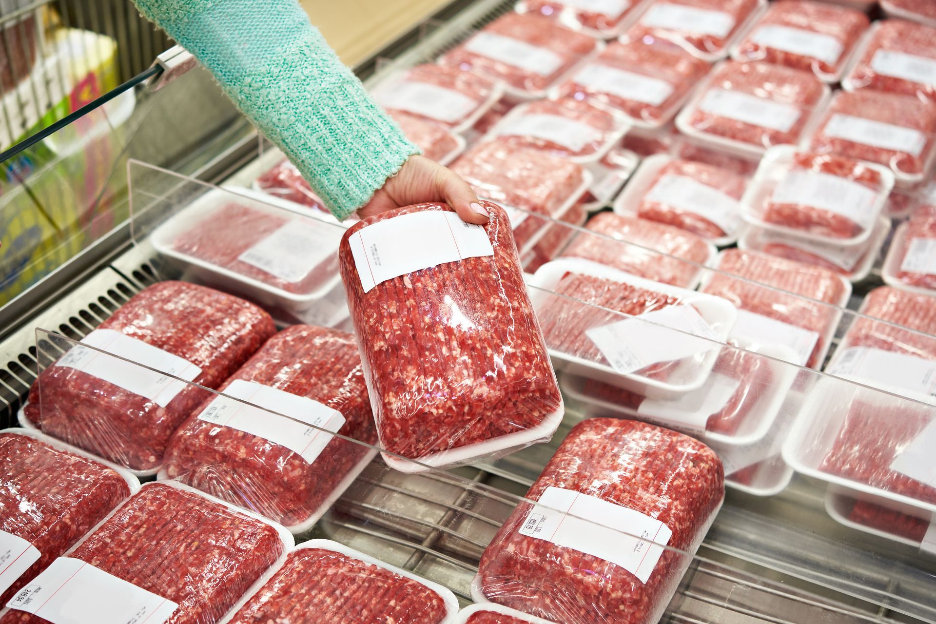 Hand placing a package of ground meat in a supermarket freezer display