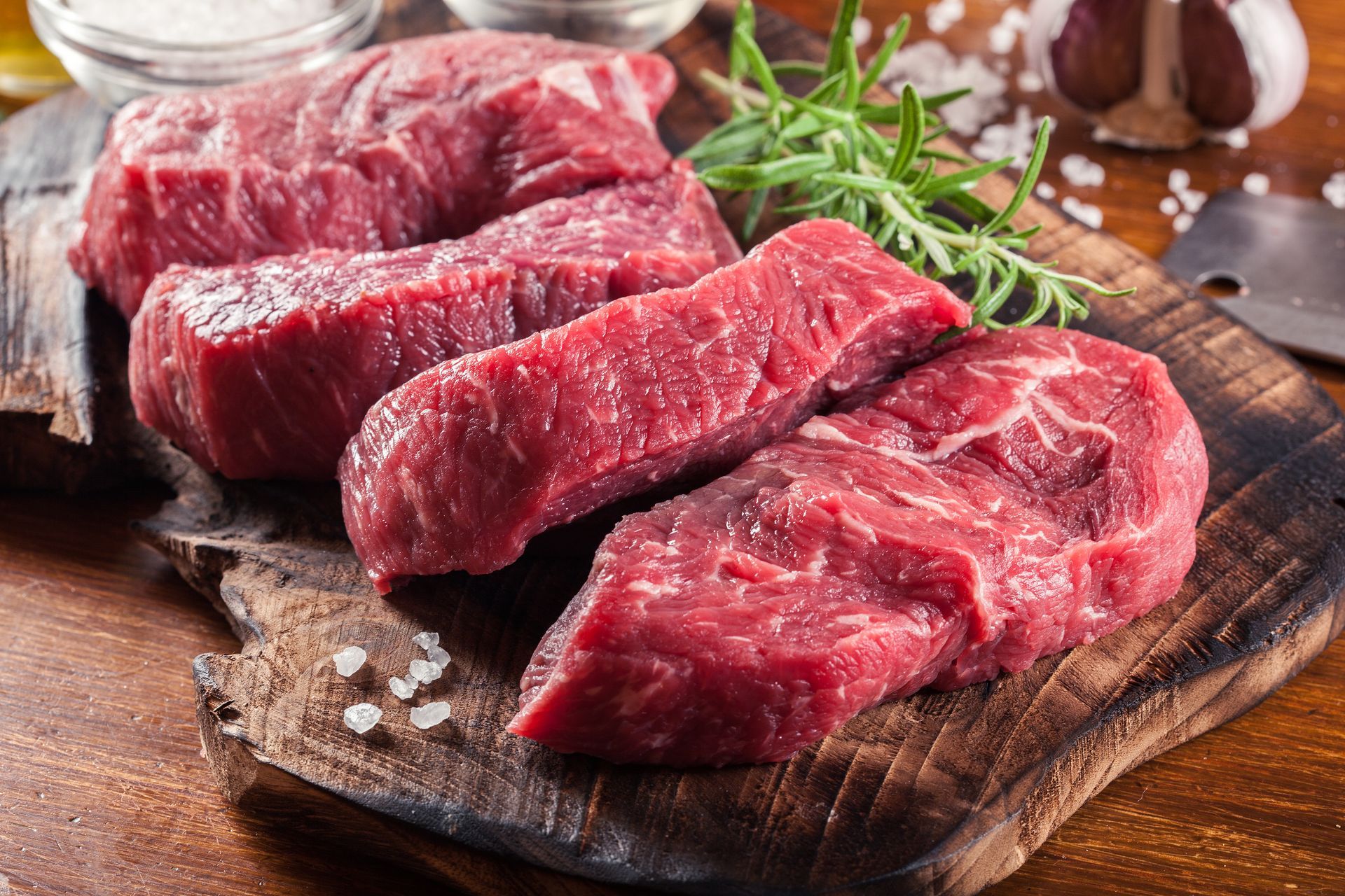 Raw beef steaks on a wooden cutting board with rosemary and coarse salt, ready for cooking