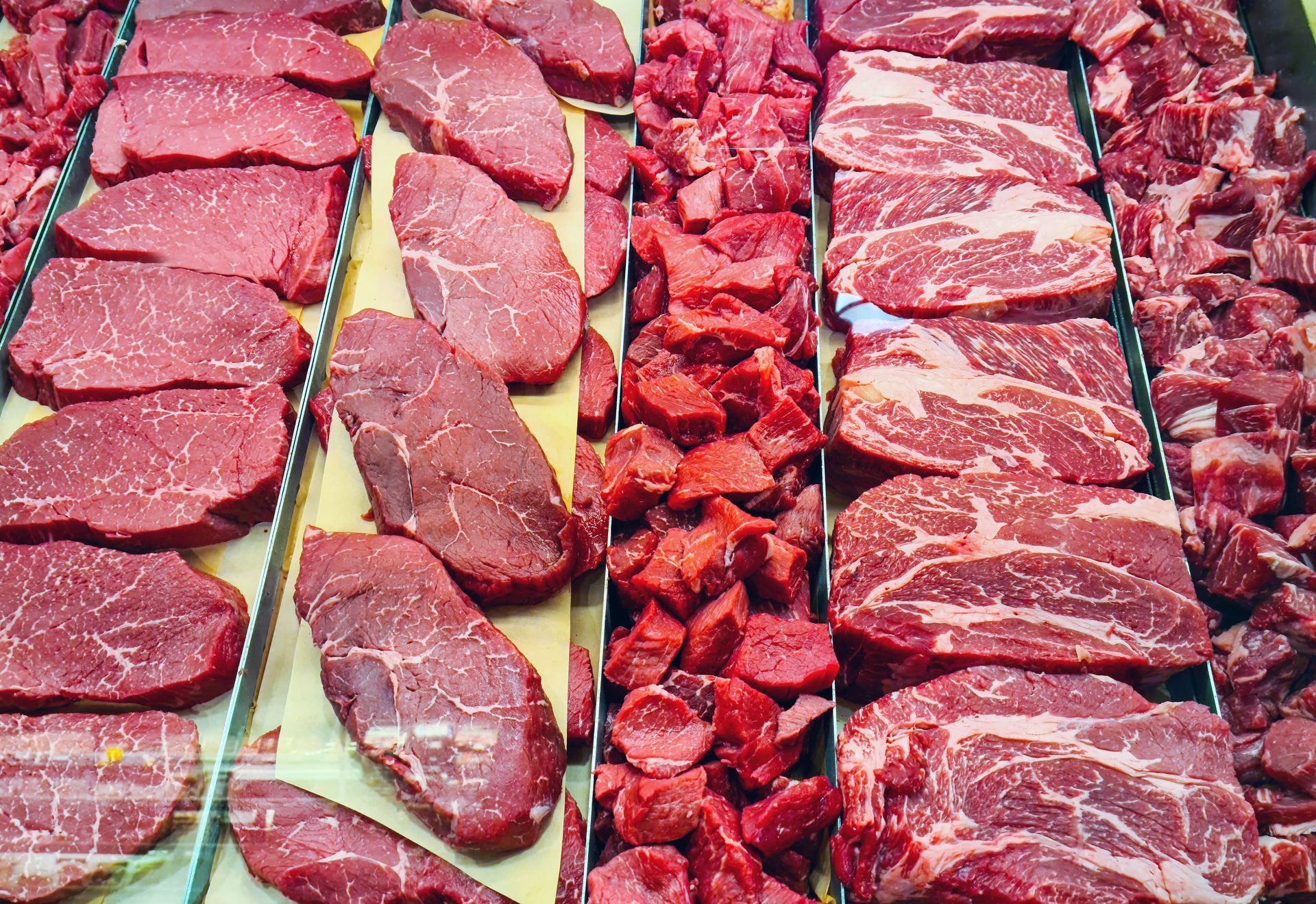 Assorted raw beef cuts displayed in rows at a butcher counter