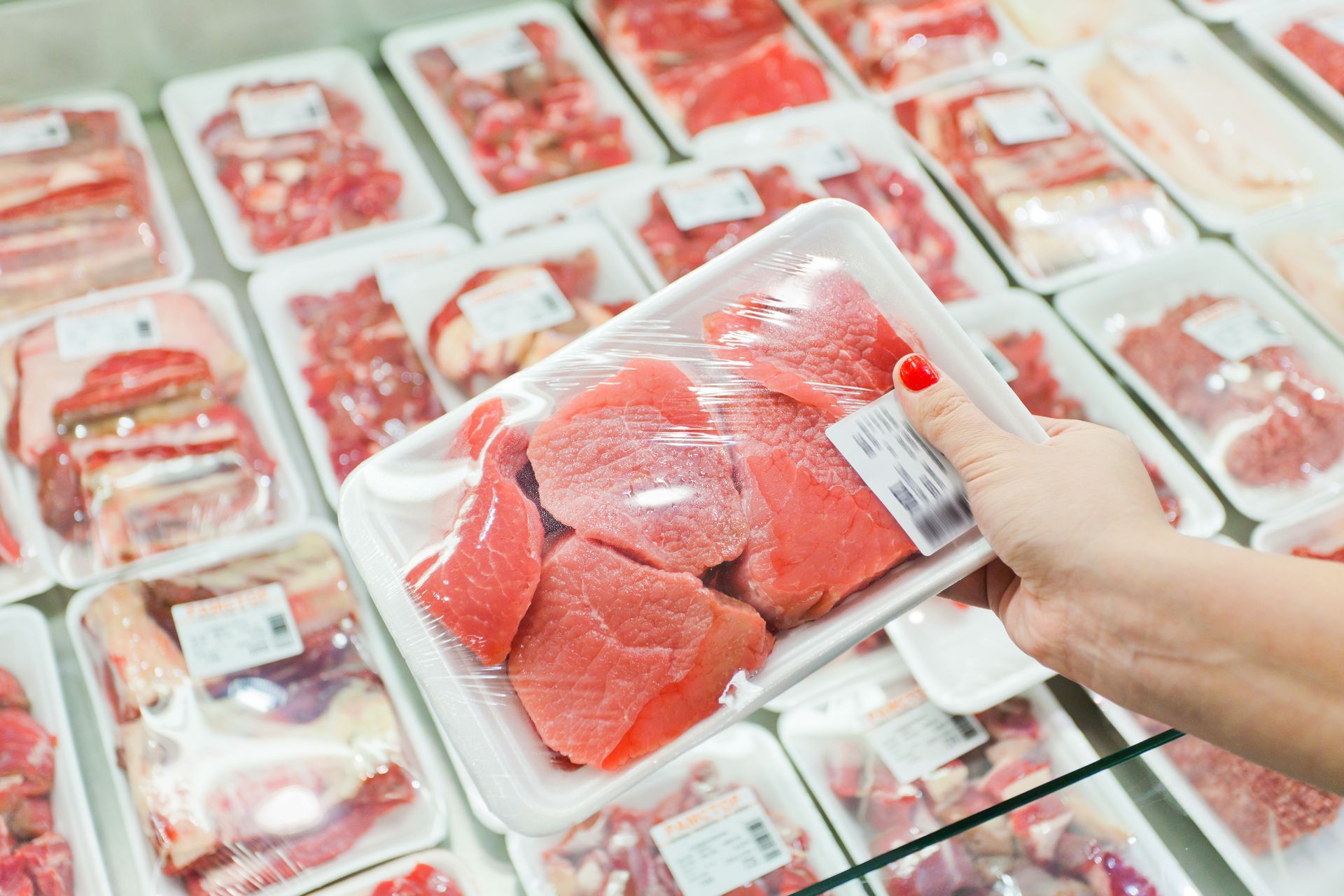 Hand holding a tray of packaged red fish fillets in a supermarket freezer section