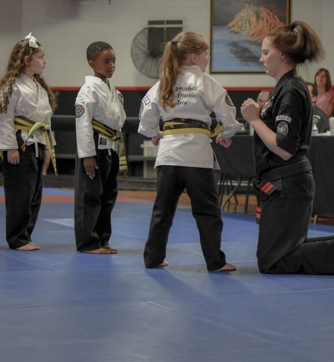 A woman is kneeling down in front of a group of children in martial arts uniforms