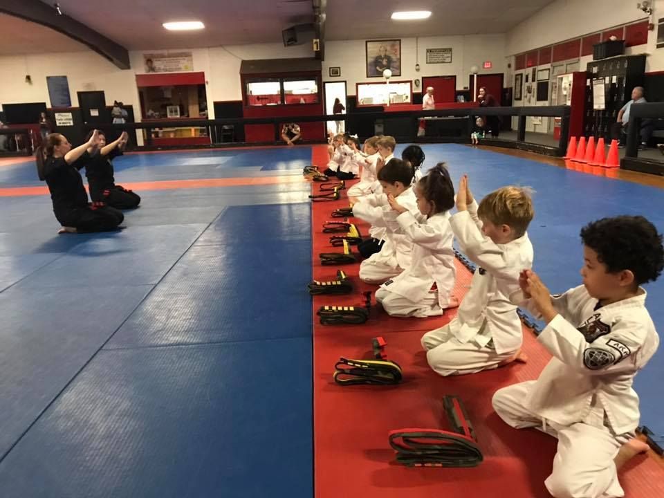 A group of children are sitting on the floor in a karate class.