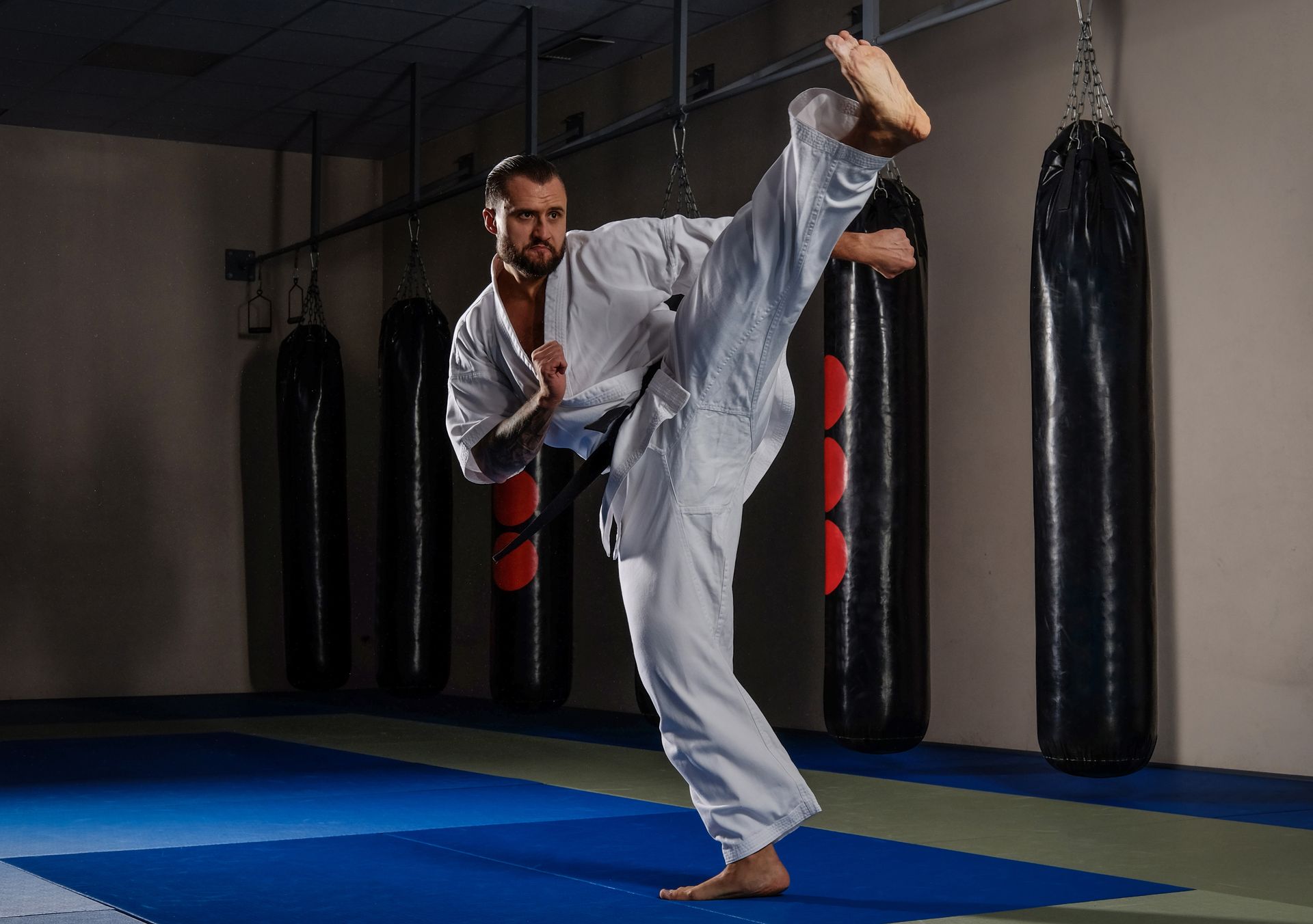 A man in a white karate uniform is kicking in a gym.