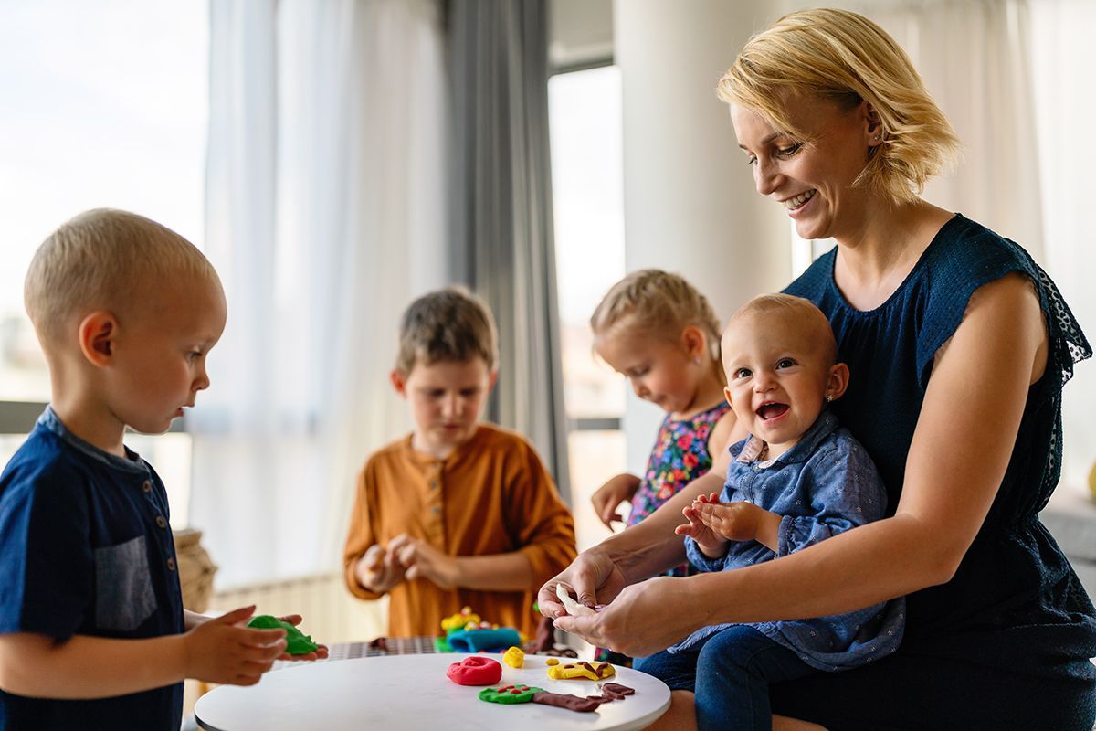 A woman is sitting at a table with three children playing with play dough.