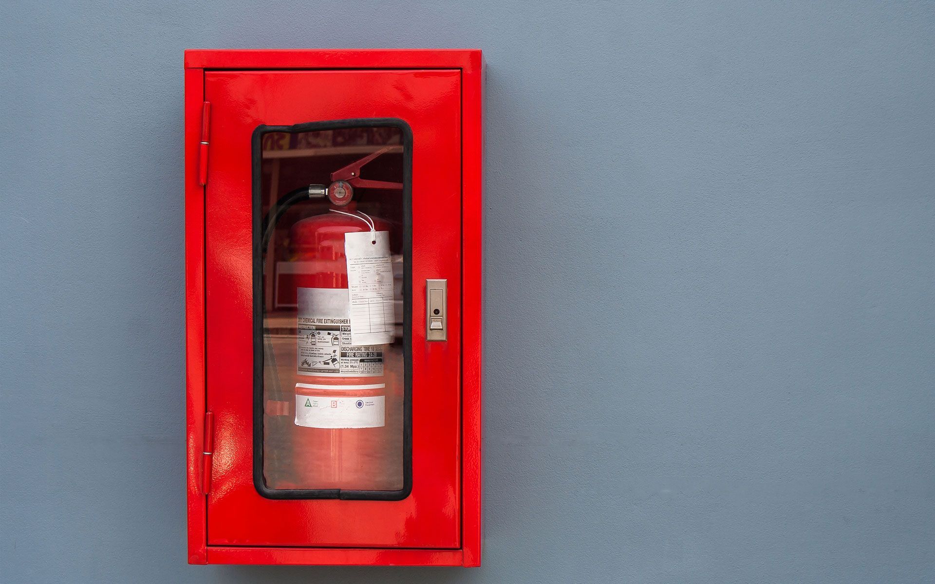 A red fire extinguisher is hanging in a red box on a wall.