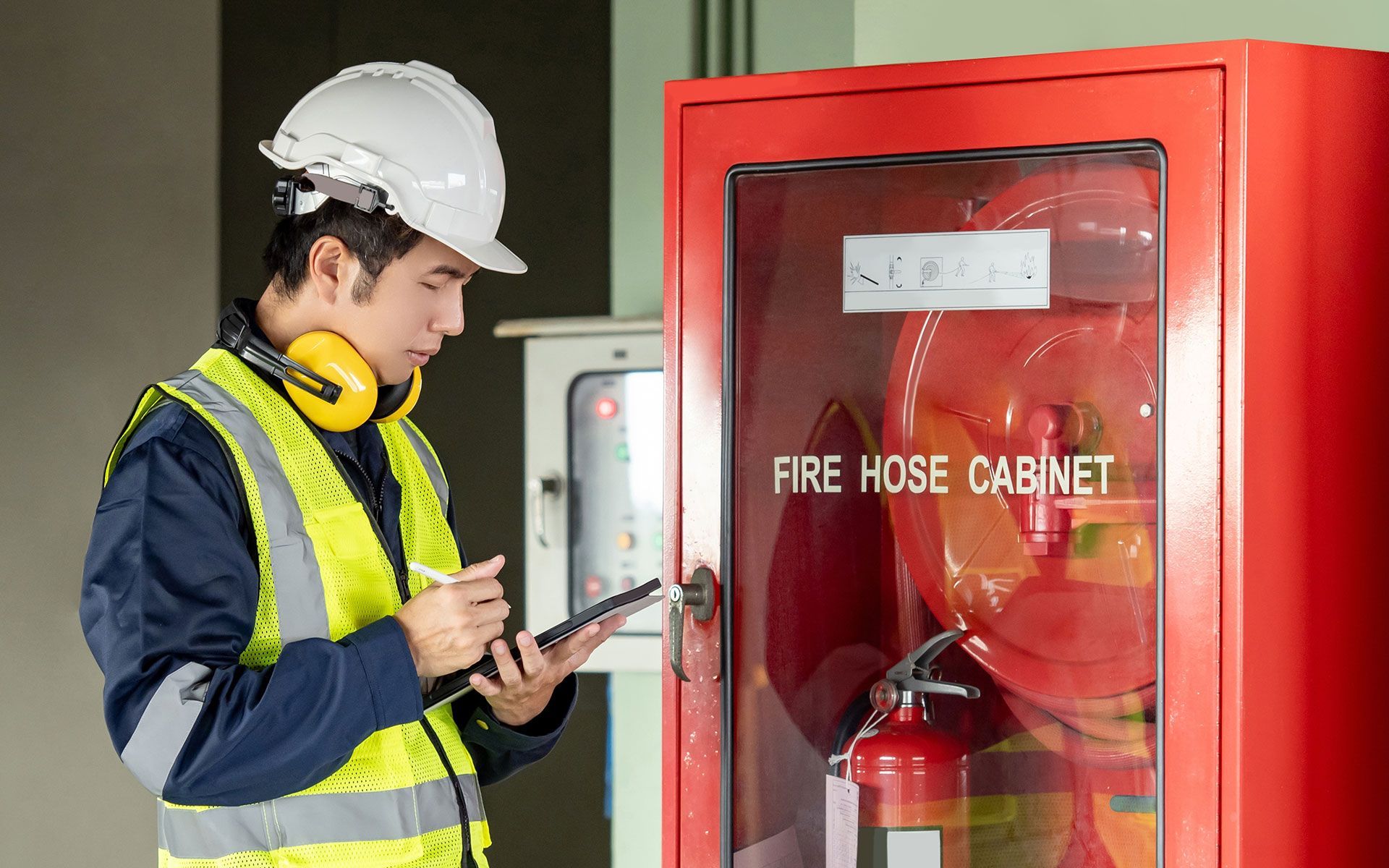 A man in a hard hat is looking at a fire hose cabinet.