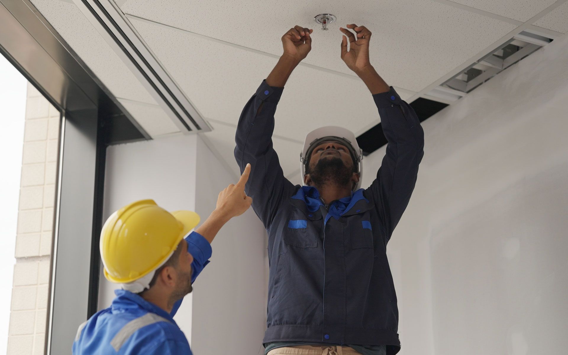 Two men in hard hats are working on a ceiling.