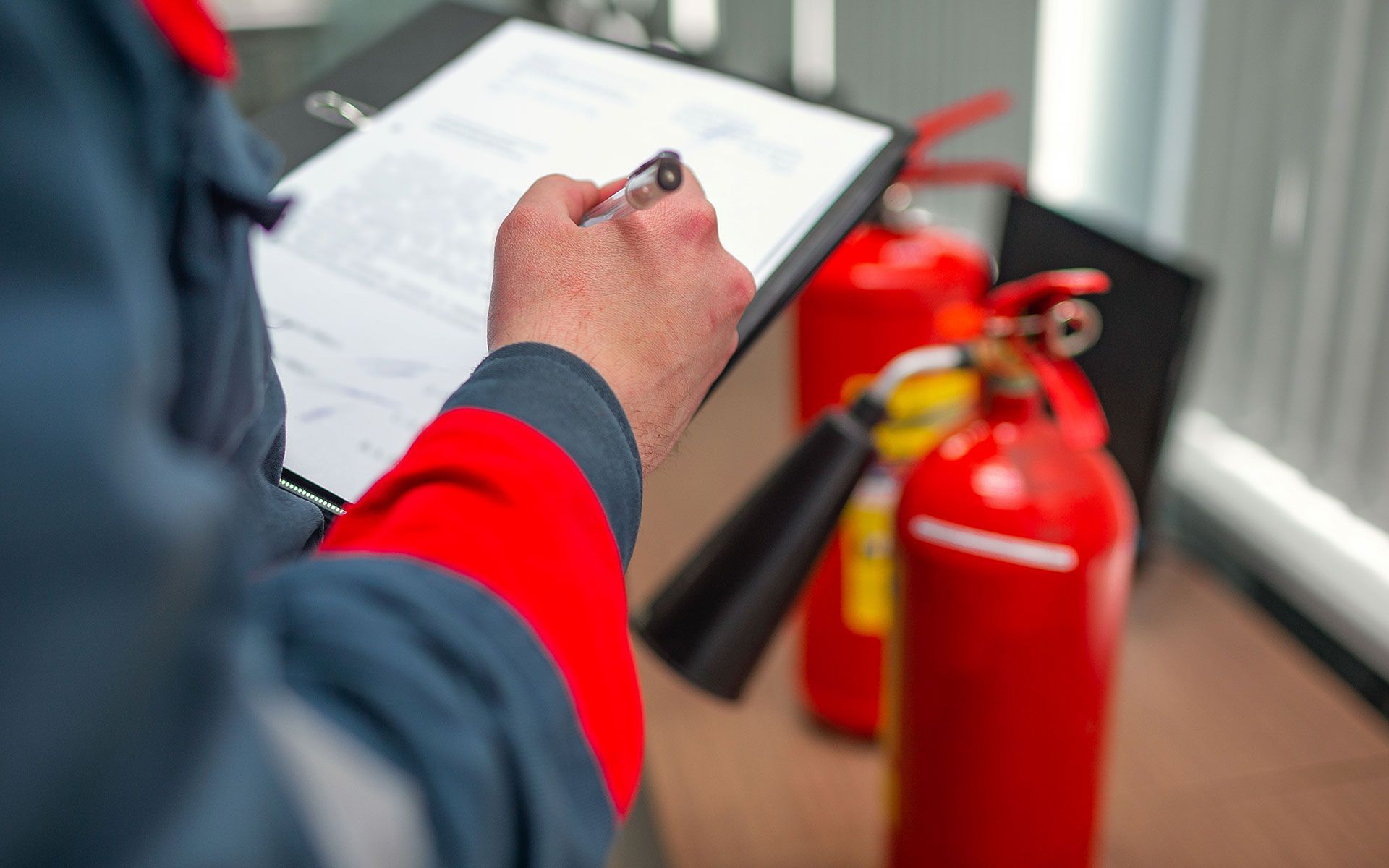 A man is writing on a clipboard next to fire extinguishers.