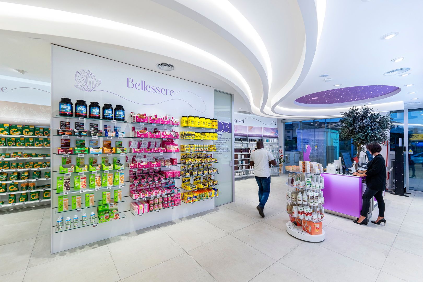 Corridoio luminoso di una farmacia o di un negozio di cosmetici con scaffali colorati e un banco cassa con due persone