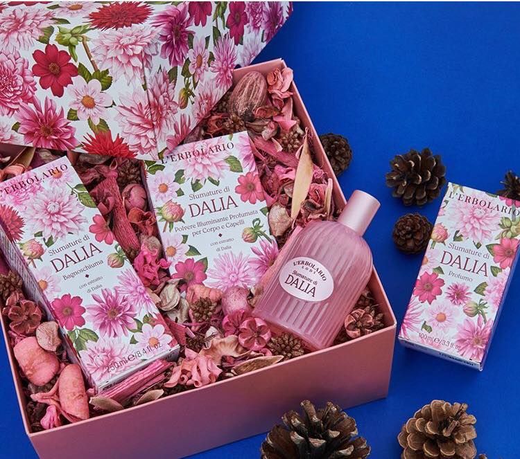 Cofanetto regalo floreale rosa con prodotti e profumo DAHLIA in una scatola rosa su sfondo blu, con pigne.
