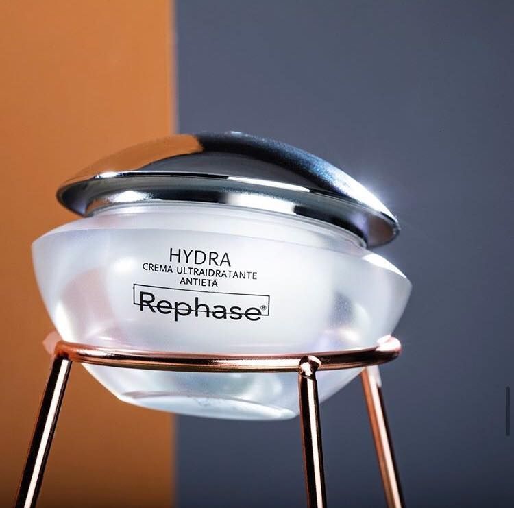Vasetto cosmetico Hydra Rephase su supporto dorato su sfondo arancione e grigio