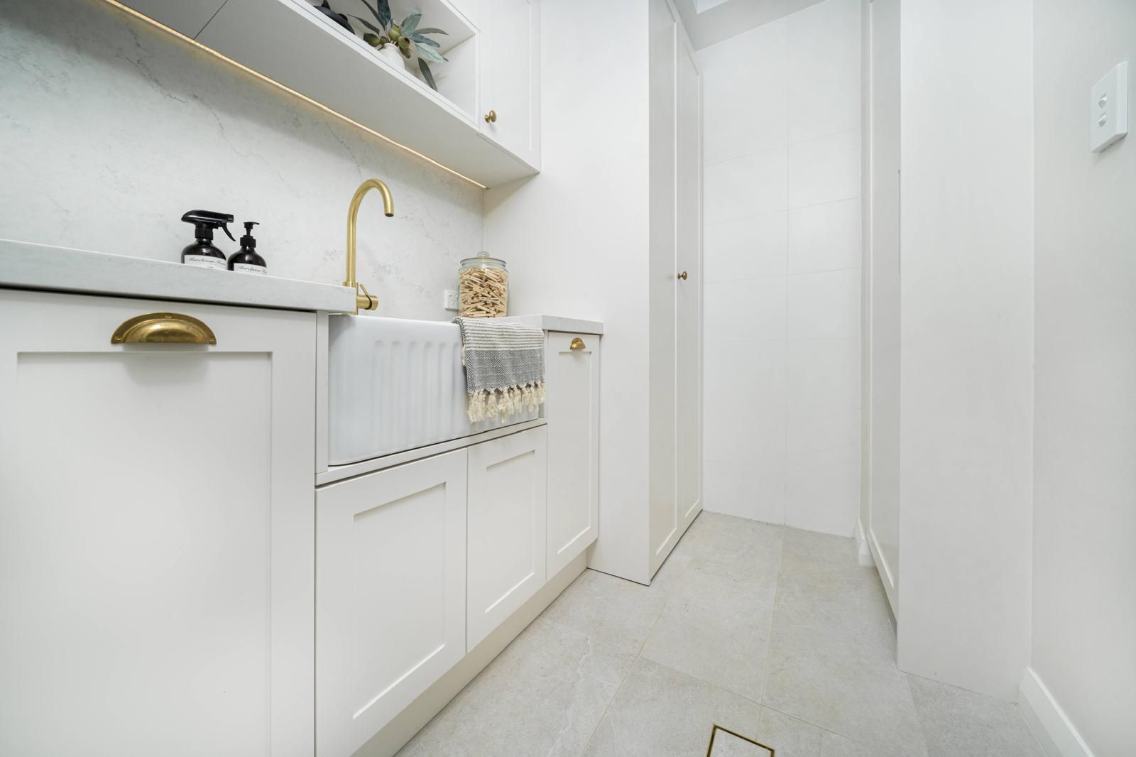 Modern white bathroom with farmhouse sink, brass faucet, built-in cabinets, soft lighting, tiled floor