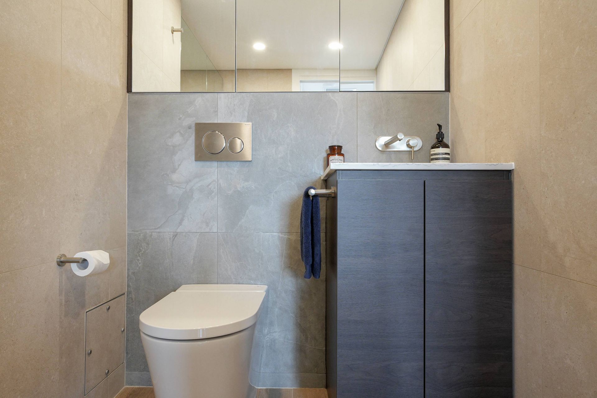 Modern small bathroom layout in Sydney featuring a wall-hung toilet, grey tiles, and a dark vanity
