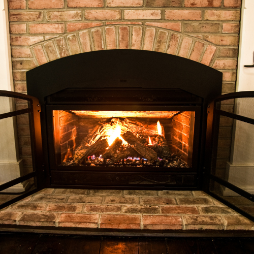 A lit fireplace with an arched black metal insert, surrounded by brick masonry.