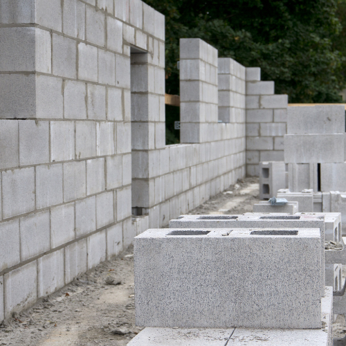 A partially constructed concrete block wall at a building site, with stacked blocks in the foreground.