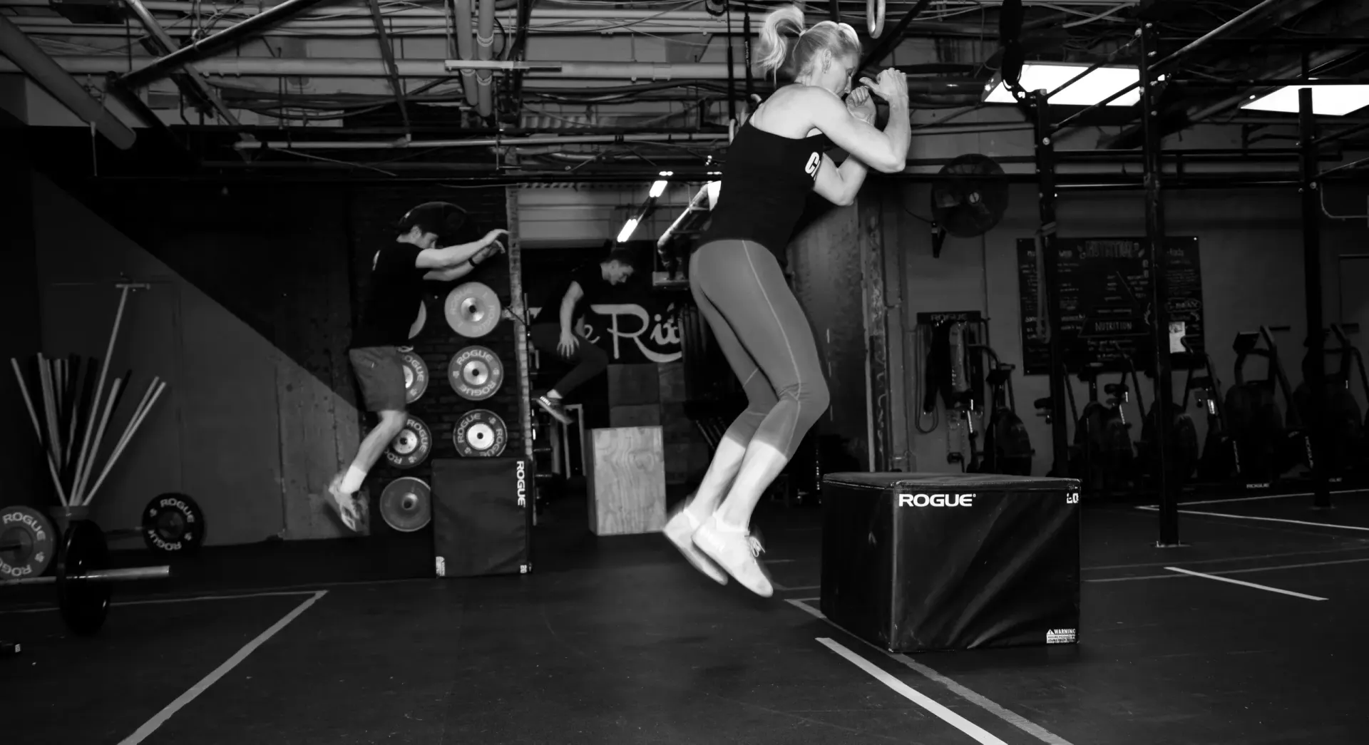 A woman is jumping over a box in a gym.