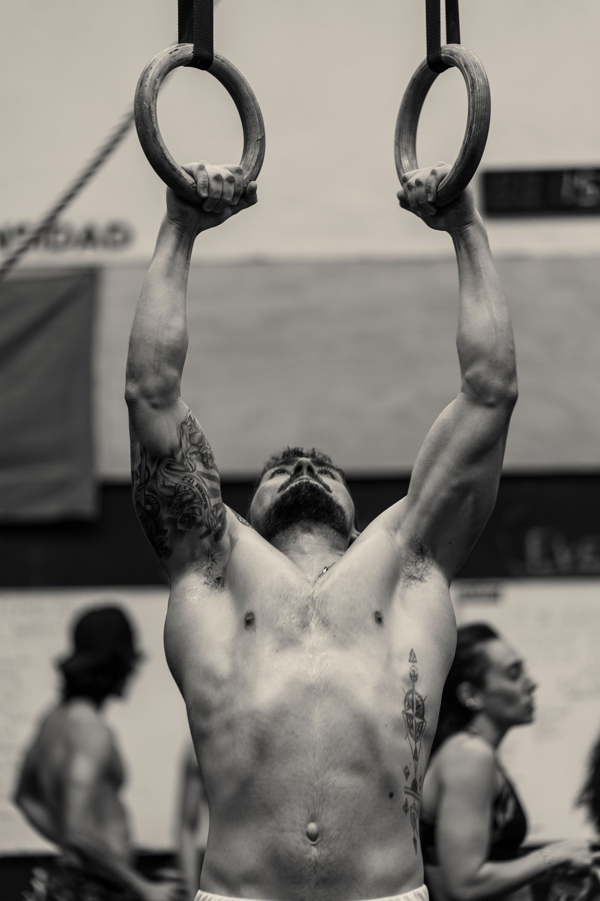 Athlete hanging from gymnastic rings with arms extended overhead in a gym setting