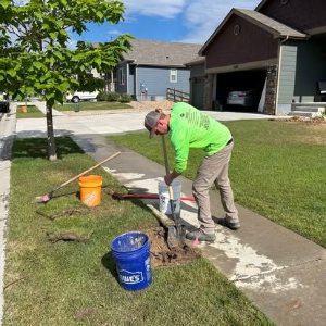 Worker using a jackhammer to break concrete on a sidewalk beside a lawn and driveway