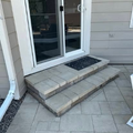 Front door with concrete steps, black doormat, and tan siding patio entrance