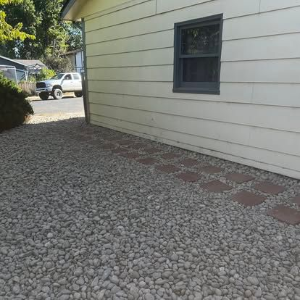 Gravel side yard beside a beige house with a narrow brick path and a window.