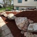 Landscaped yard with large rocks, red mulch, and a stone walkway beside a house