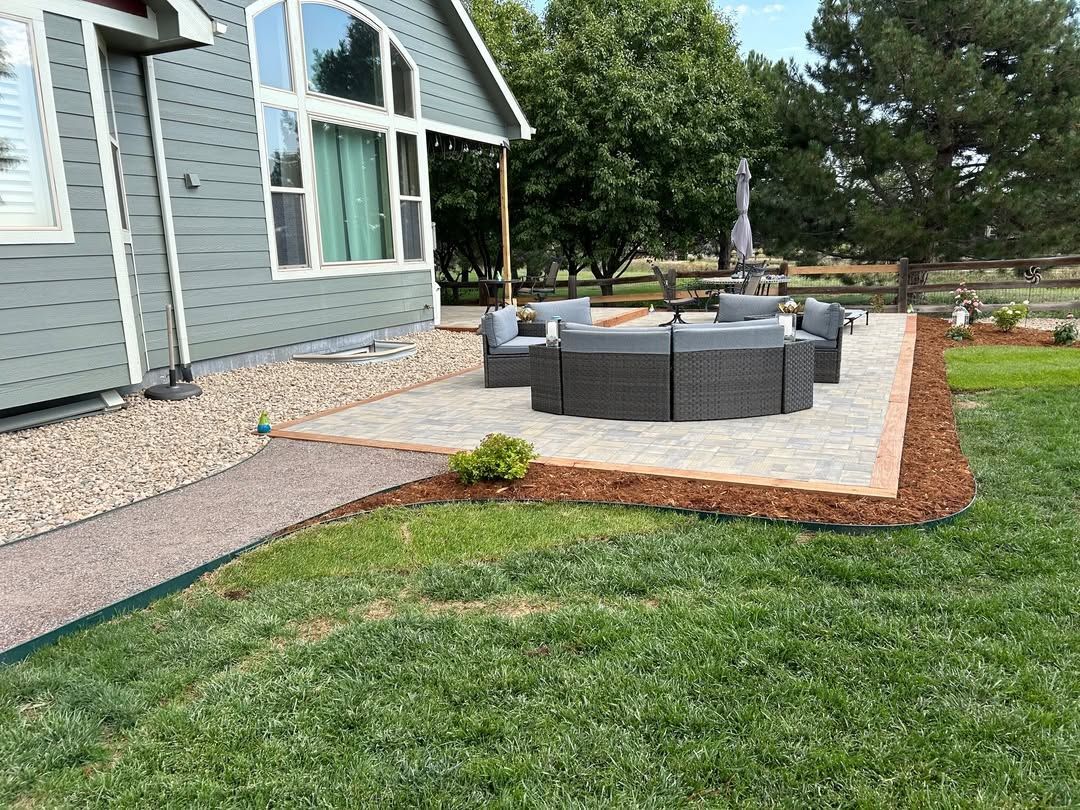 Backyard patio with gray outdoor sofa, concrete seating area, and green lawn beside a house