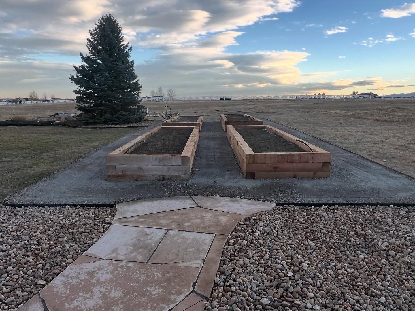 Two raised wooden garden beds on a concrete pad with a walkway, set in an open field at sunset