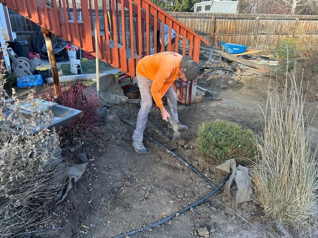Person in orange jacket working in a dirt garden beside red stairs.