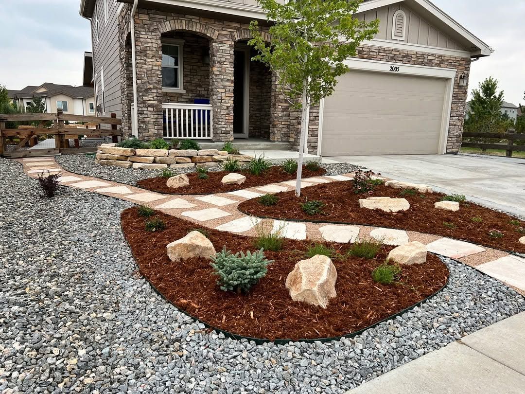 Front yard landscaping with stone walkway, mulch beds, gravel, and a house with a garage