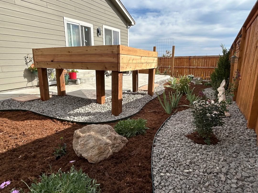 Backyard landscape with raised wooden deck, gravel paths, rocks, mulch, and a fence