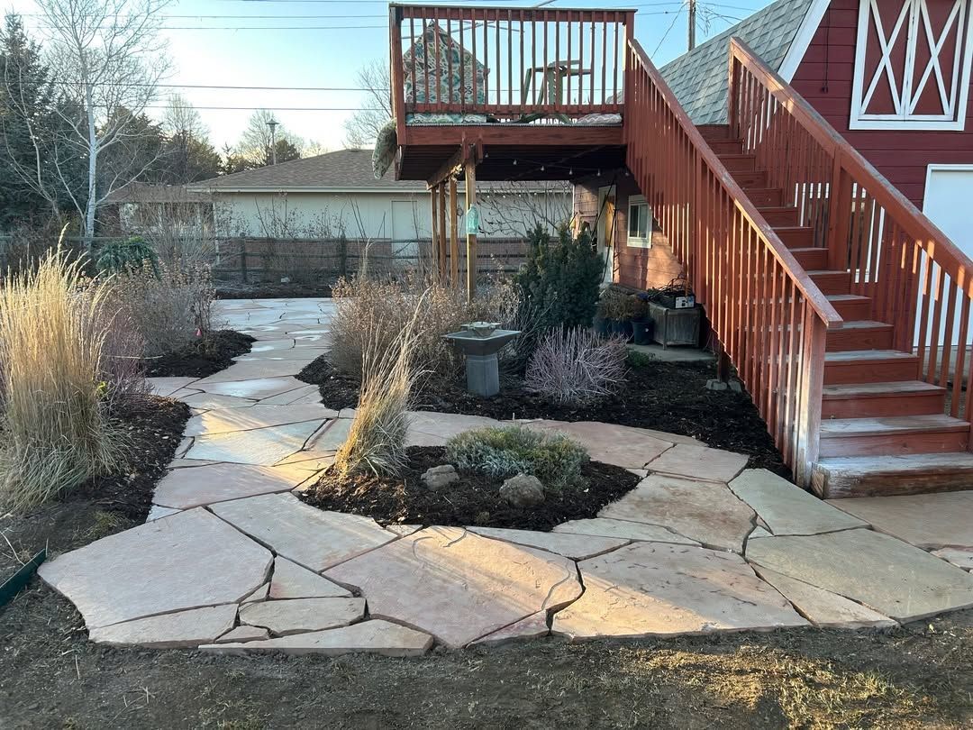 Stone patio with raised wooden deck stairs leading to a backyard garden path and pond area