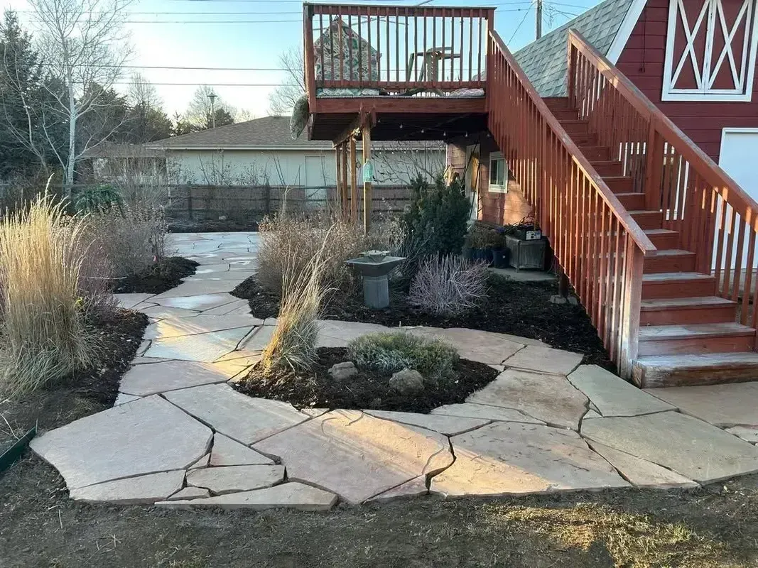 Stone patio with raised wooden deck stairs leading to a backyard garden path and pond area