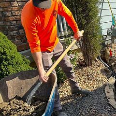 Worker in orange shirt shoveling gravel in a landscaped garden bed