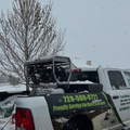 White pickup truck with green landscaping sign in snowy scene, parked by a bare tree.