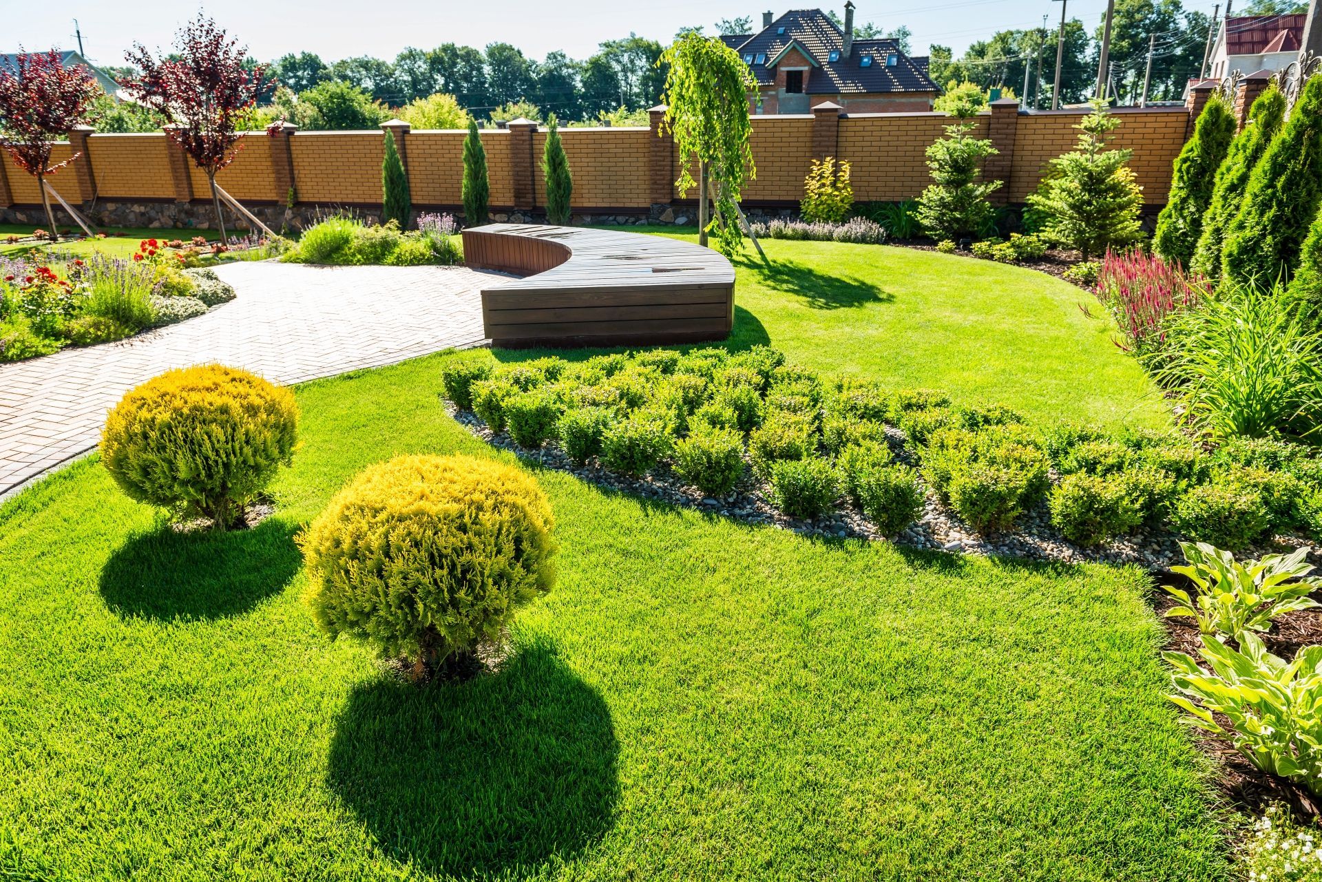 Well-maintained landscaped backyard with curved bench, shrubs, and neatly trimmed green lawn.