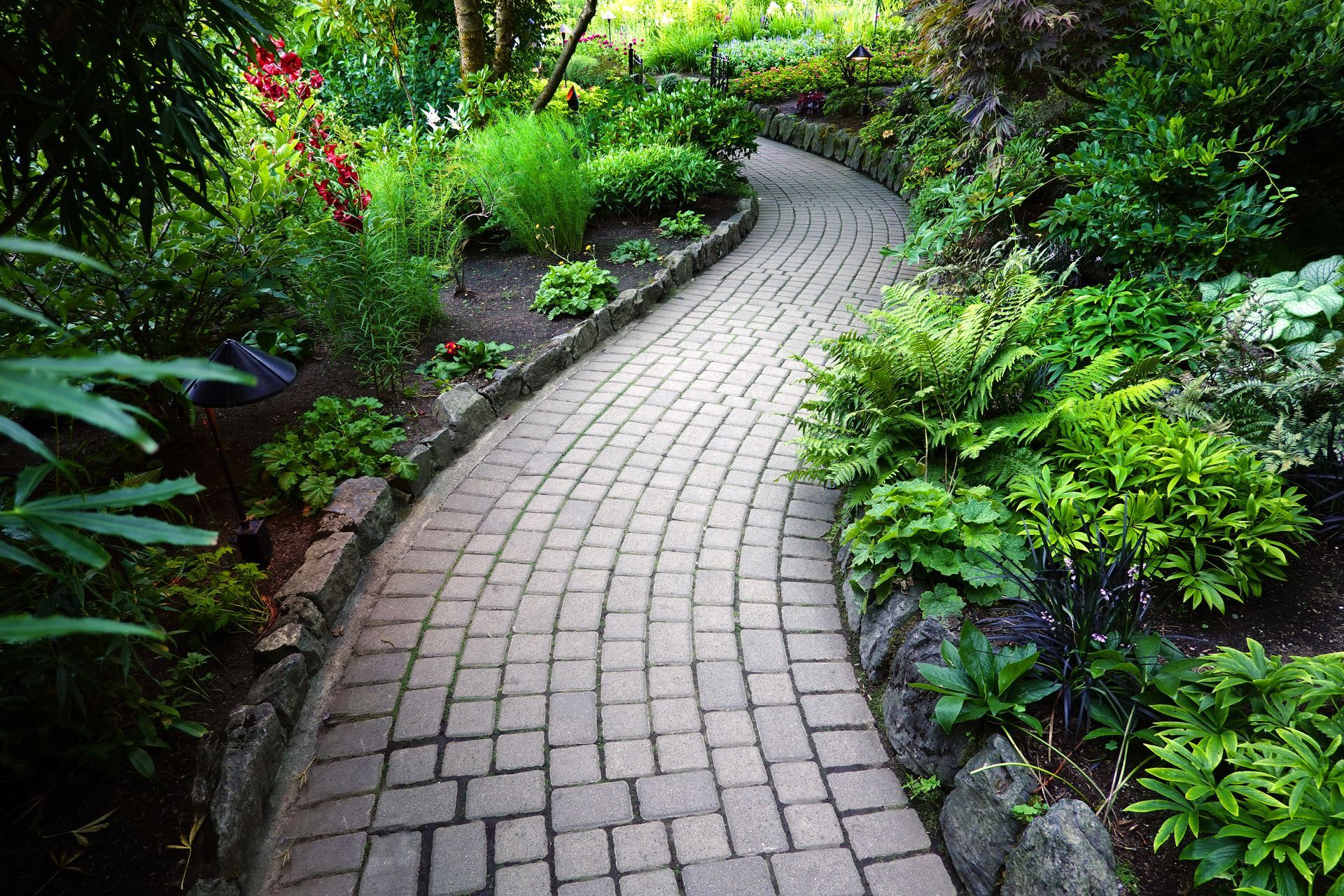 Curved stone pathway through a lush green garden with modern black lights. Curved stone pathway through a lush green garden with modern black lights.