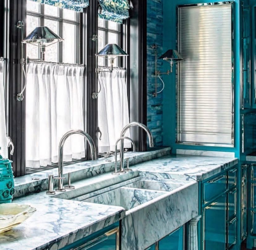 A kitchen with two sinks , two windows and a marble counter top.