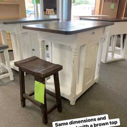 A wooden stool is sitting next to a white table with a brown top.