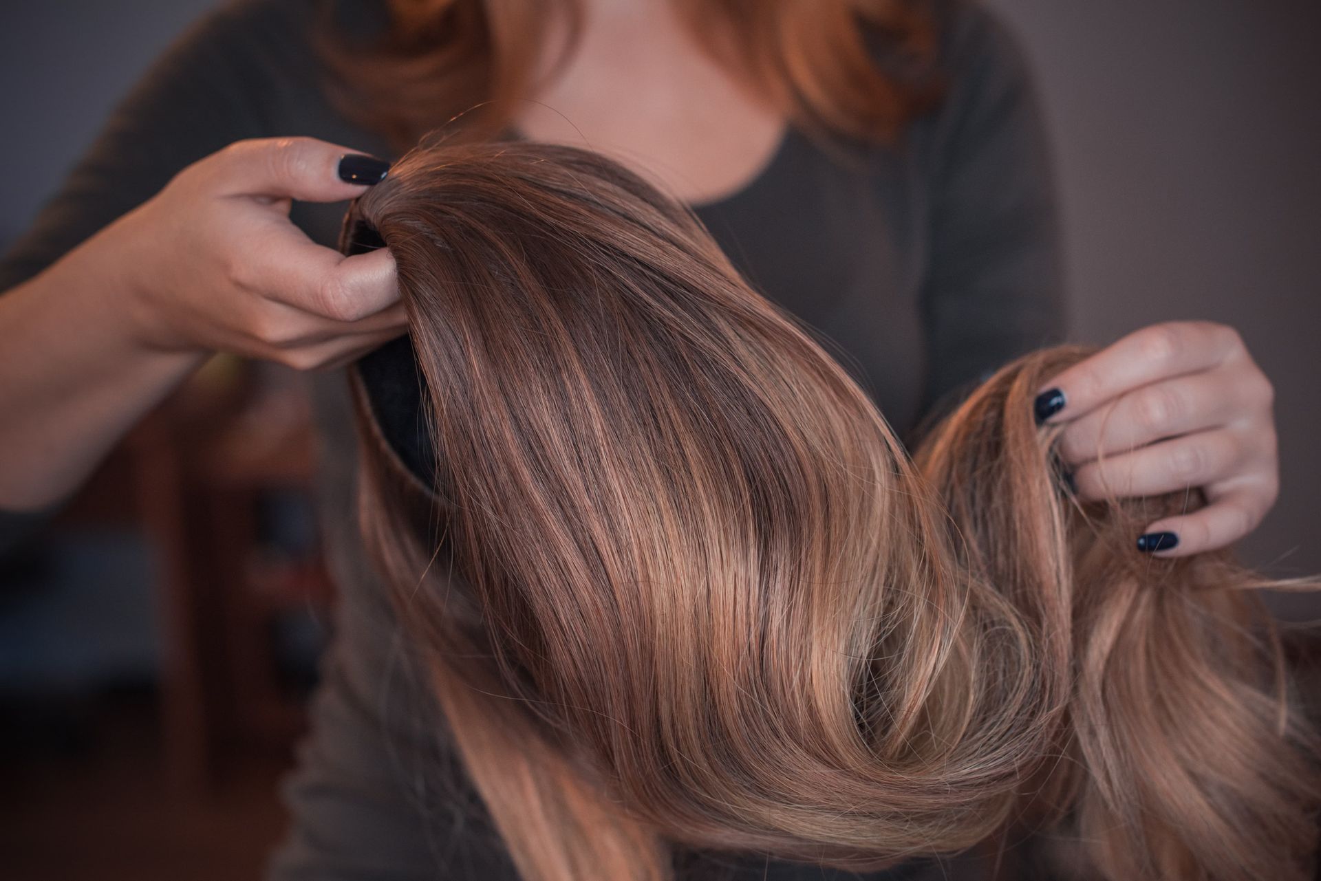 Hands holding long, wavy brown hair in a close-up hair styling scene