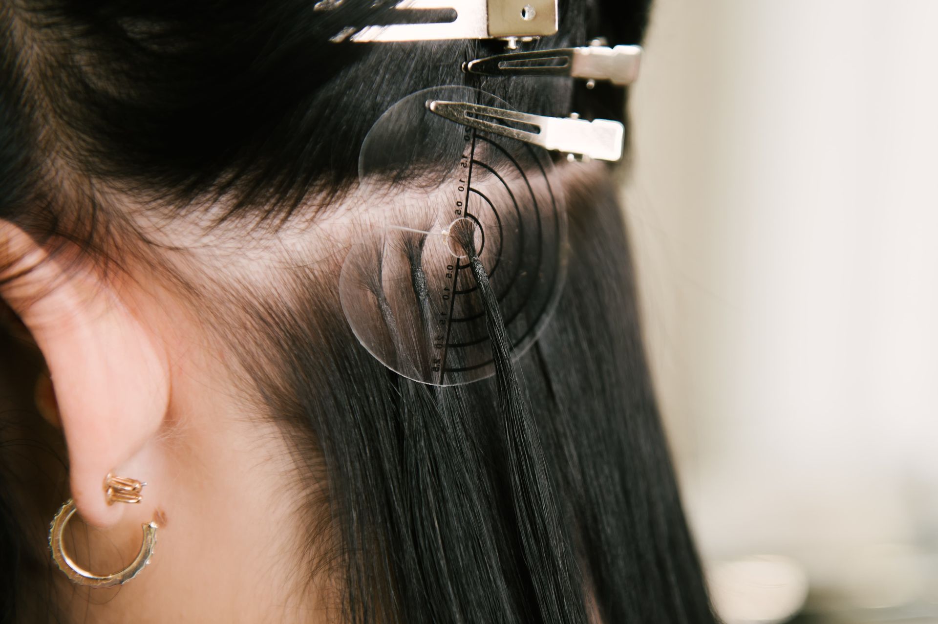 Hair extension being attached with a clamp near an ear, close-up view
