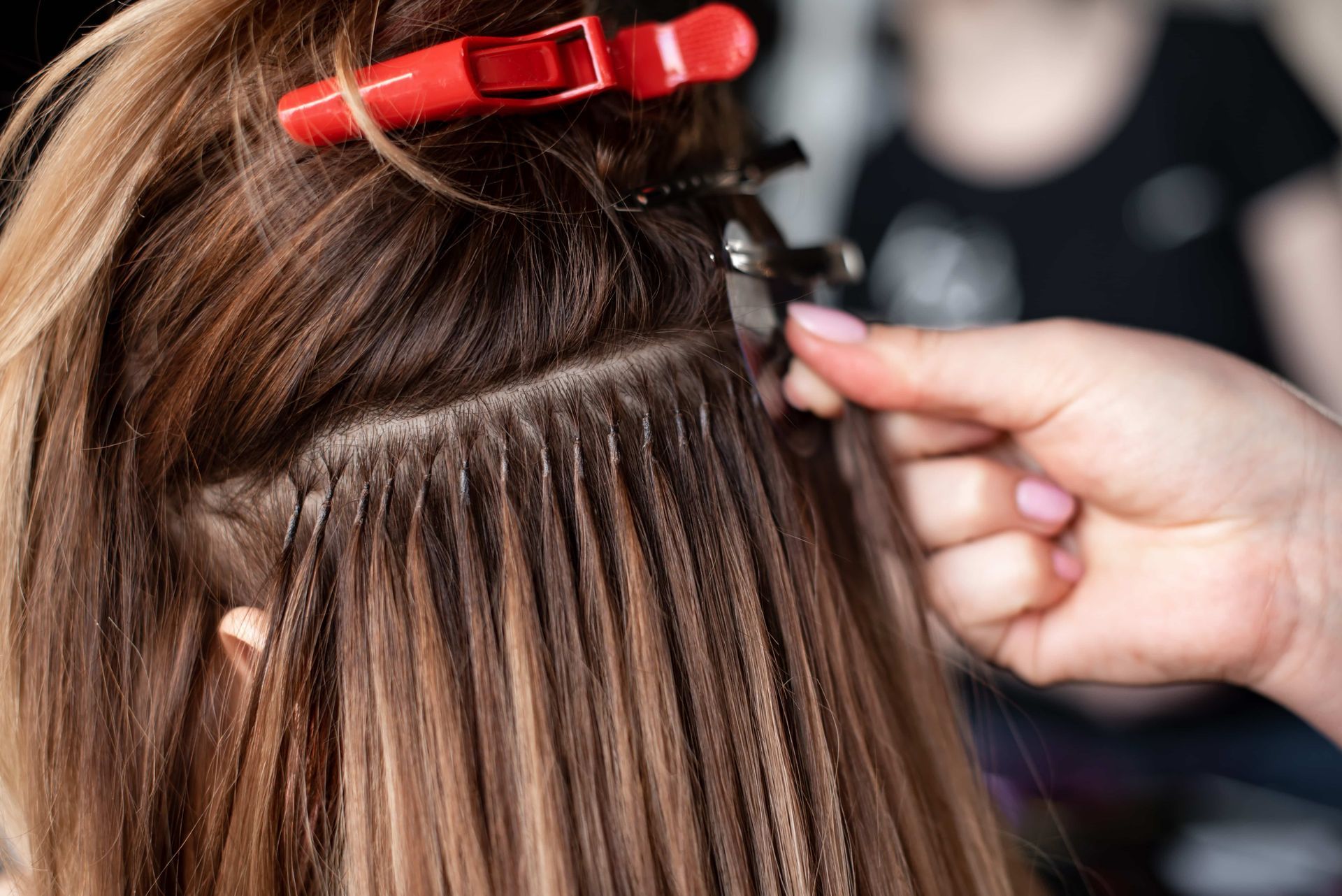 Hair being sectioned with a red clip while a hand parts the strands