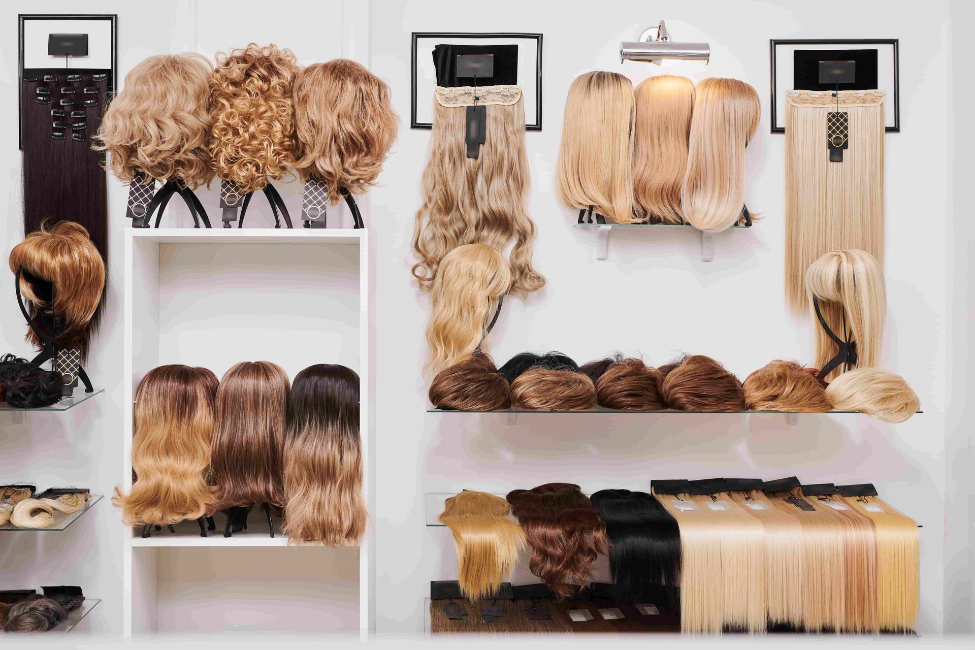 Hair extension display with multiple blonde and brown hairpieces on white shelves and wall hooks