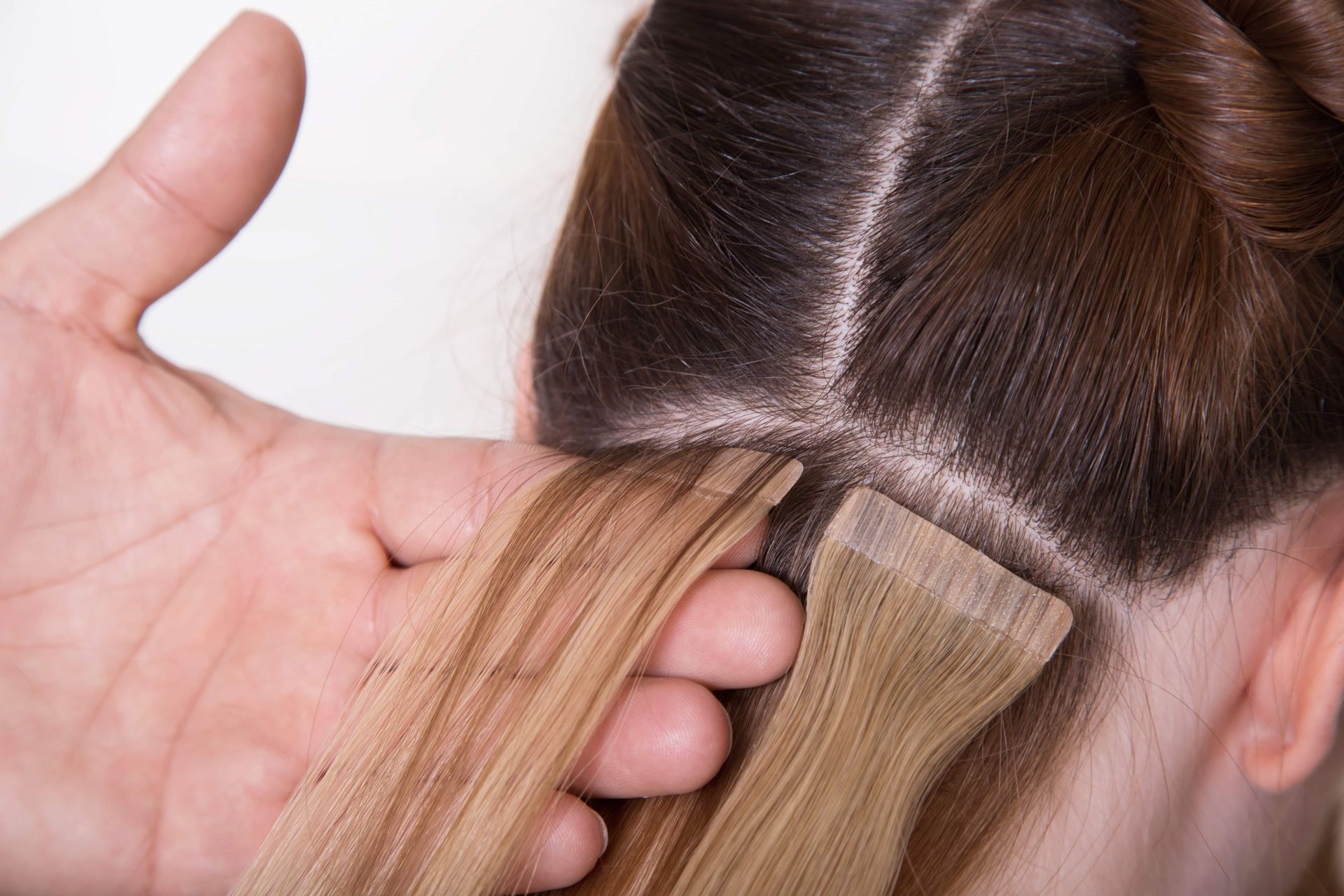 Hairdresser applying blonde extensions to dark brown hair at the scalp sectioning line