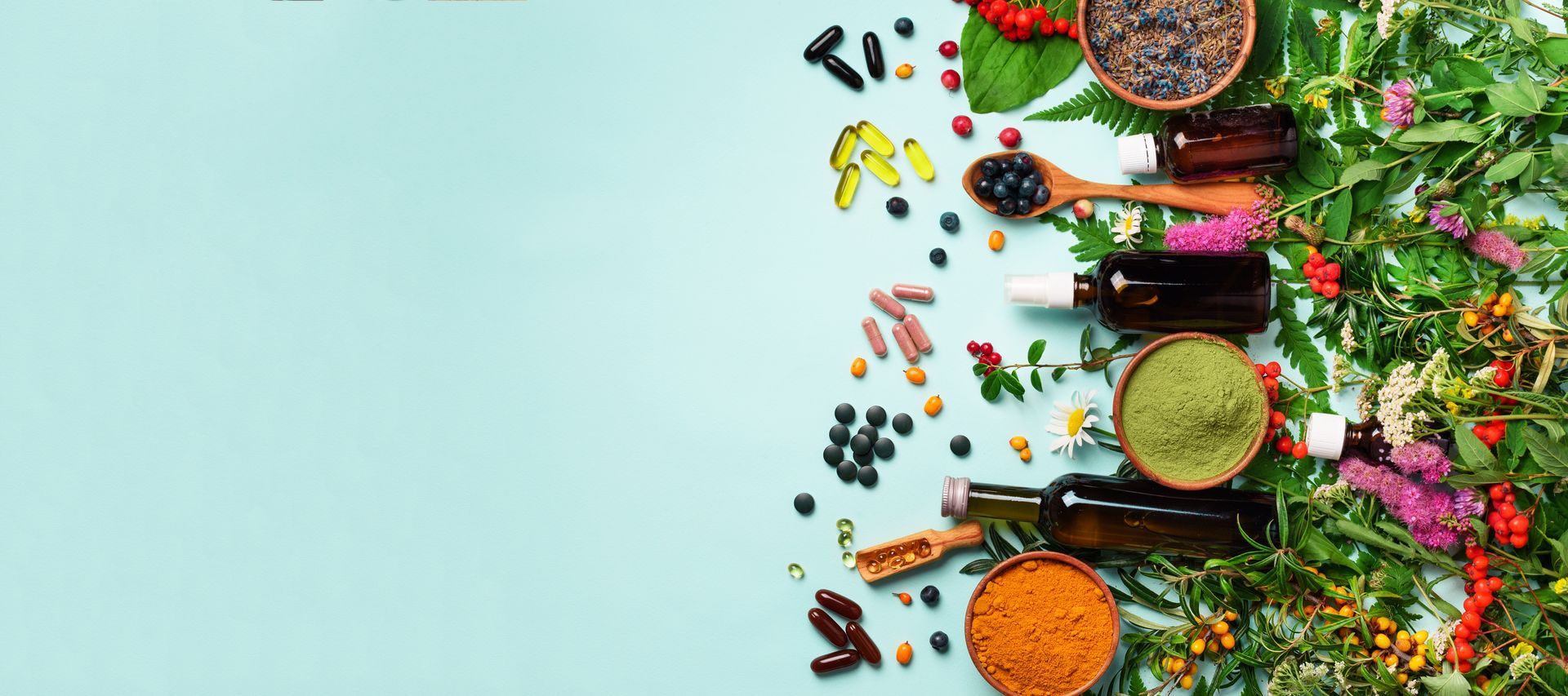 Man lies face down on a massage table while a professional places an acupuncture needle in his back. Top-down view of colorful spices, herbs, and flowers arranged on the right over a mint background