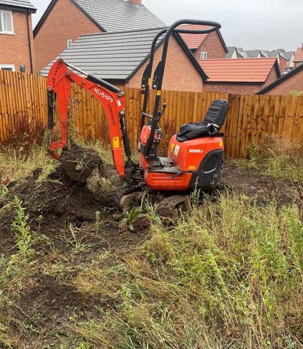 A small red excavator is digging a hole in a field.