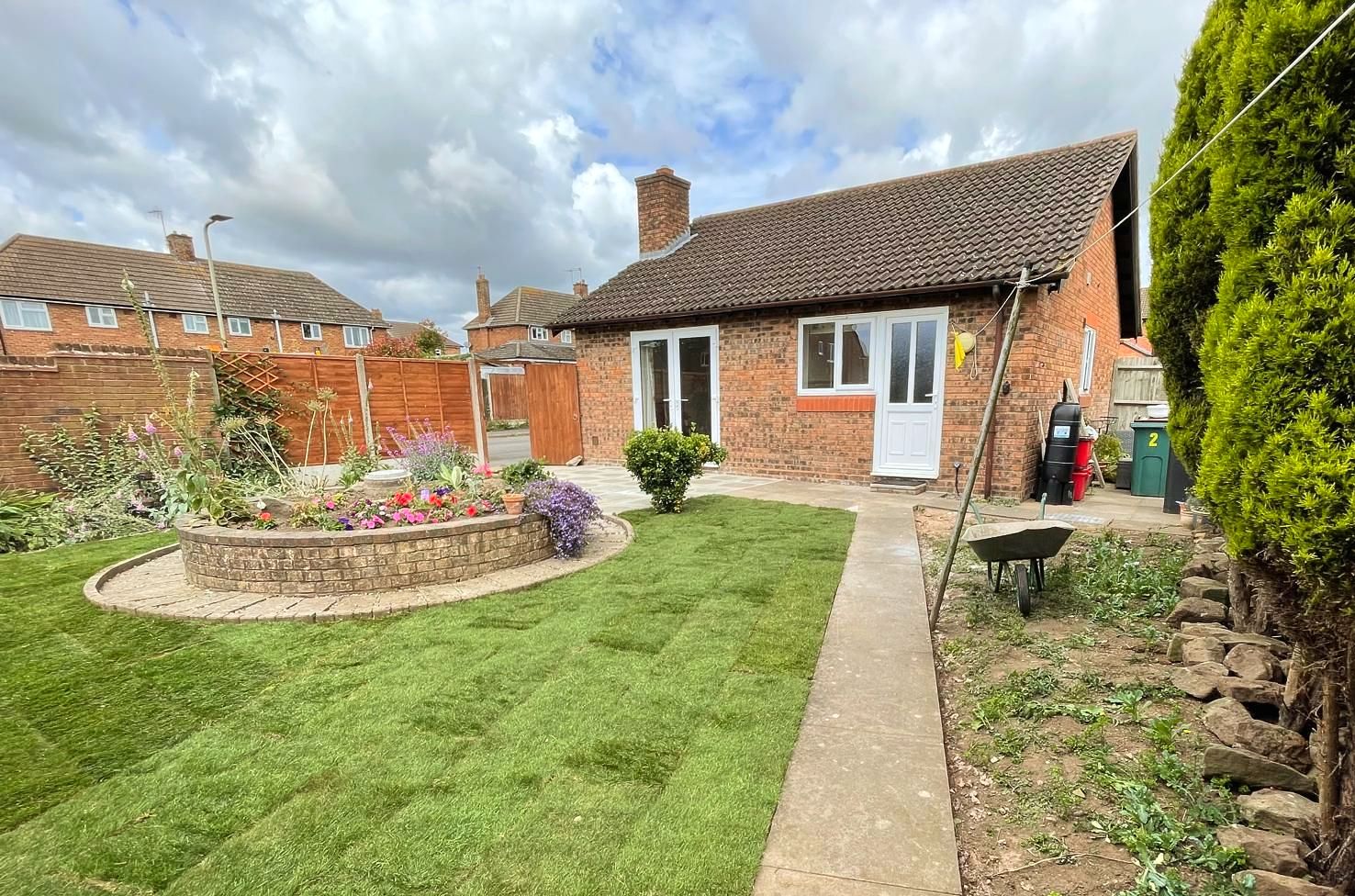 A small brick house with a large lush green garden in front of it.