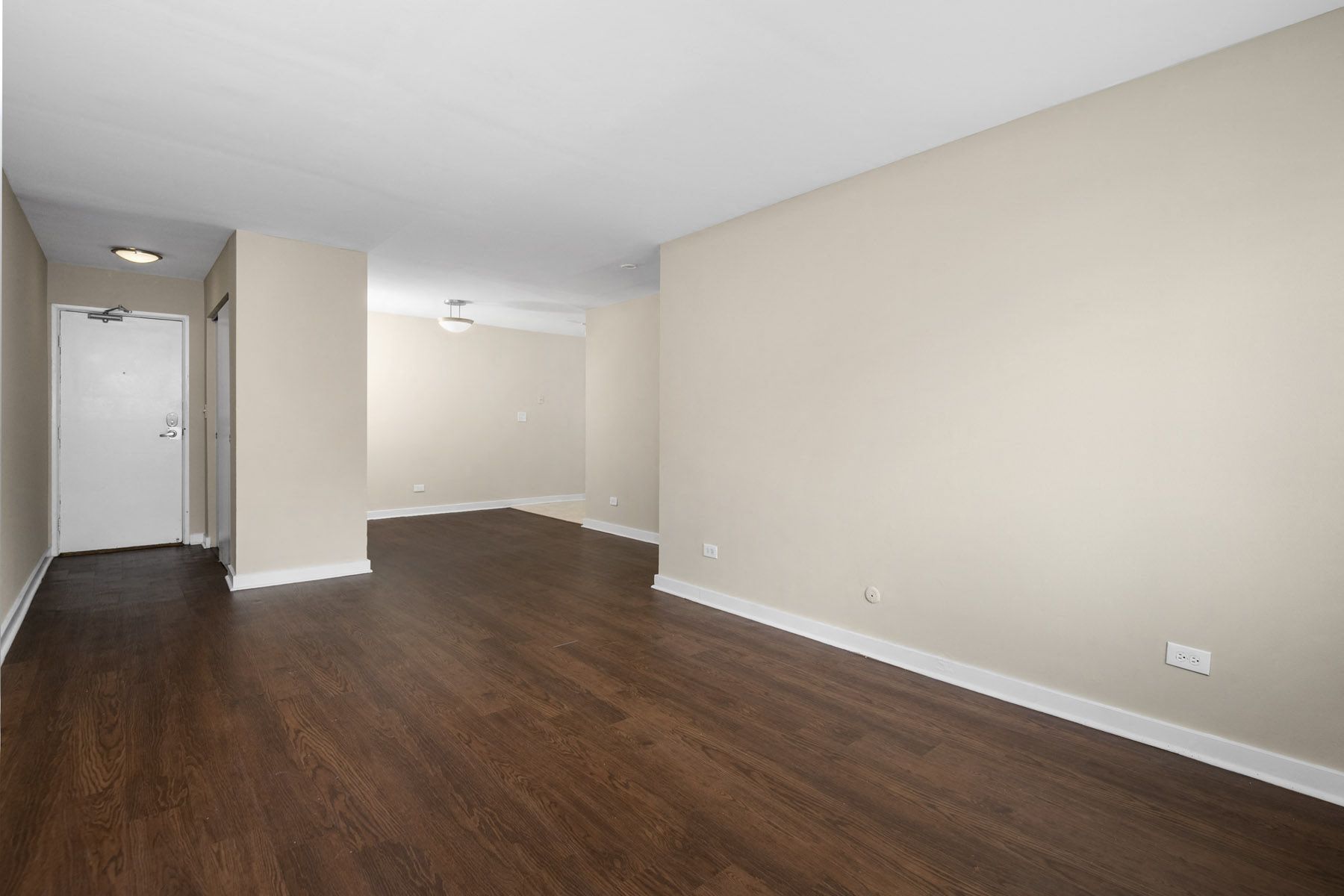 Interior view of an empty apartment living room with dark hardwood floors and beige walls.