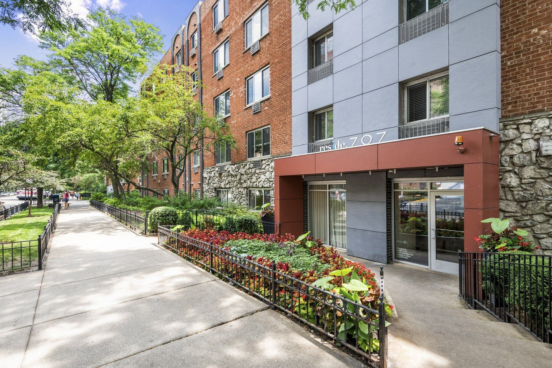 The entrance to a brick apartment building with a modern gray facade and landscaping.